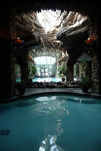 Piscine intérieure avec ouverture au toit sous forme de roche et petites cascades d'eau qui tombent dans une piscine
